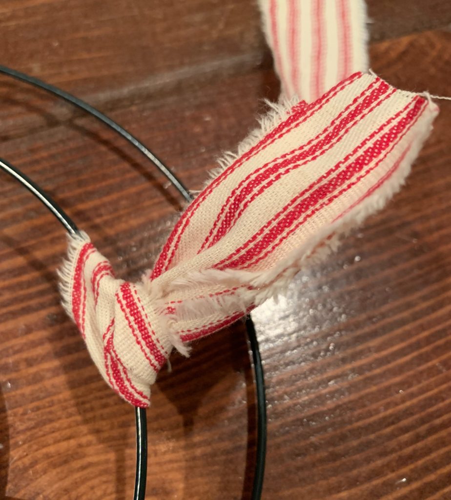 A red ticking fabric tied in a knot around a wire wreath frame. 