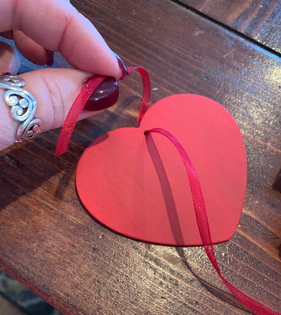 A 3 inch wooden heart painted red with a red ribbon running through it. 