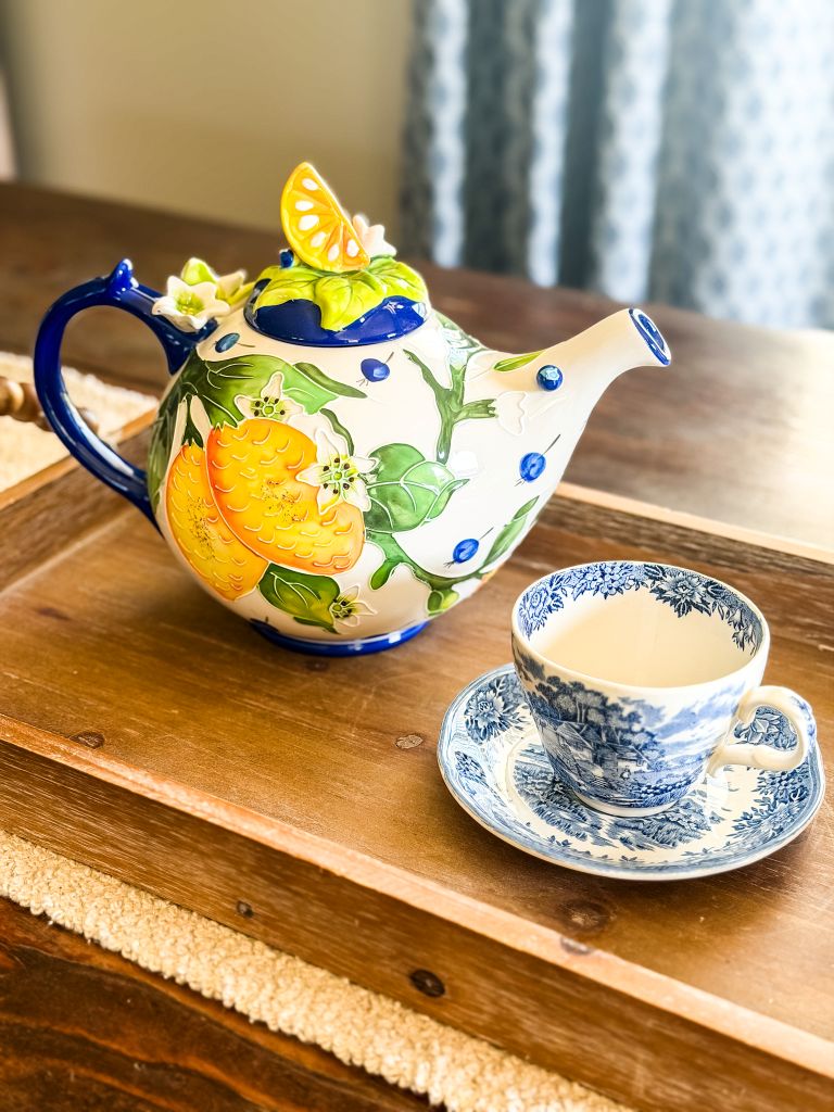 vintage blue and white floral teacup paired with a colorful citrus-themed teapot on a wooden serving tray for a cozy cottage afternoon tea party.