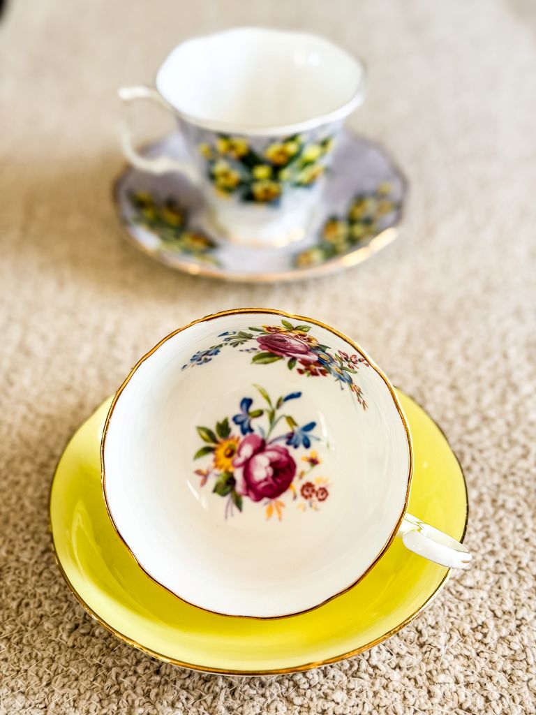 Weezie's yellow vintage teacup with floral bouquet inside, paired with a yellow saucer, with a lavender floral teacup in the background.