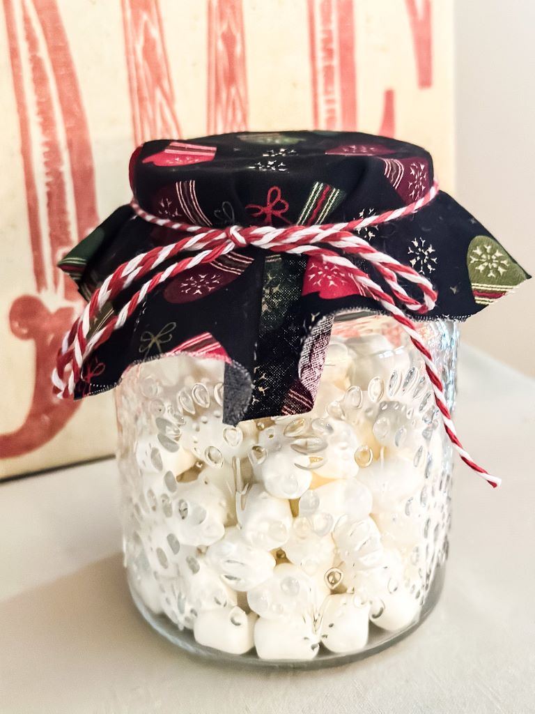 A mason jar full of small marshmallows with a fabric top secured with red and white twine.