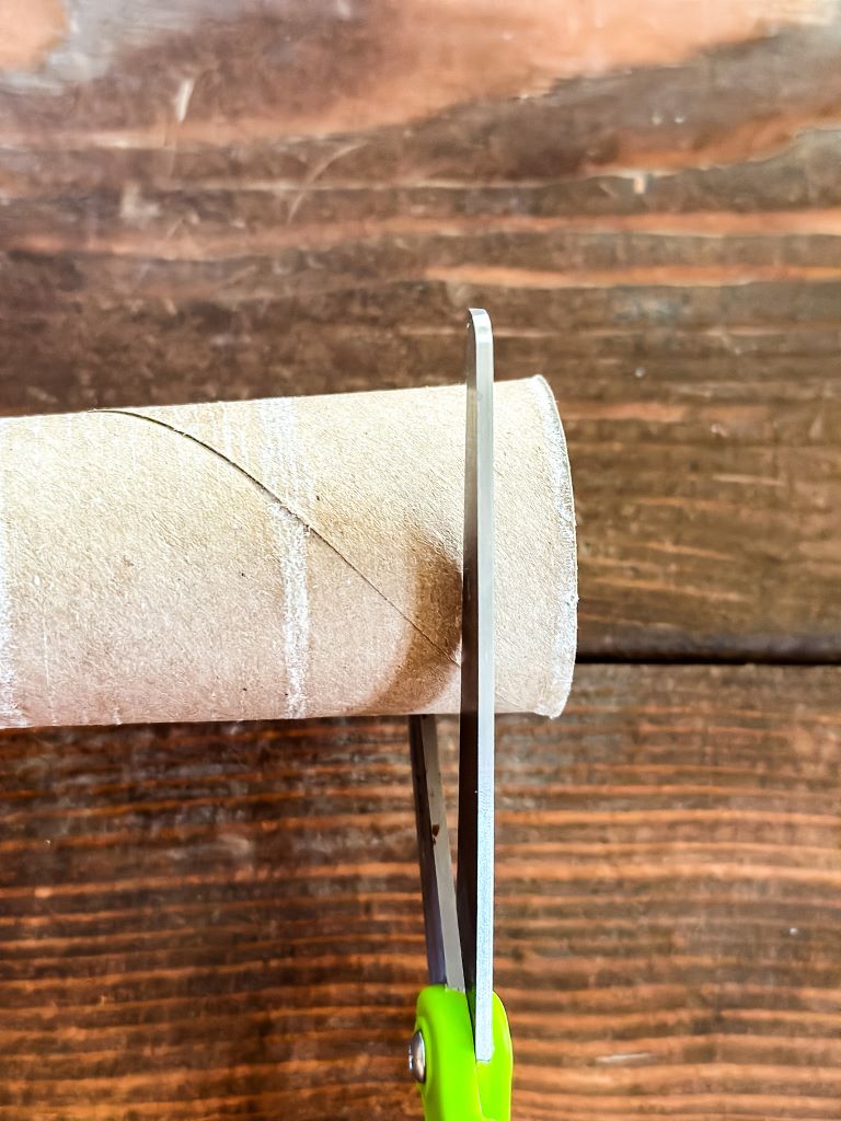 How-to DIY craft image showing the precise cutting of a cardboard tube with scissors to form the ring base for homemade rustic holiday napkin rings.