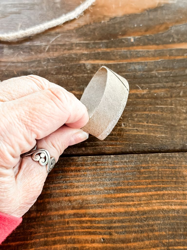 The cardboard tube cut into a small ring, forming the inexpensive, upcycled base for the rustic twine and pinecone holiday napkin rings.