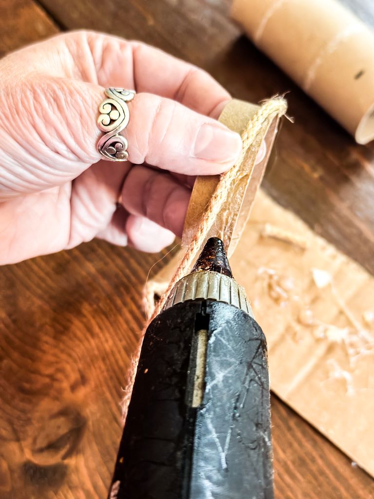 Using a hot glue gun to precisely wrap twine around a paper ring for the handmade rustic napkin ring craft; a key step in the holiday table setting DIY.