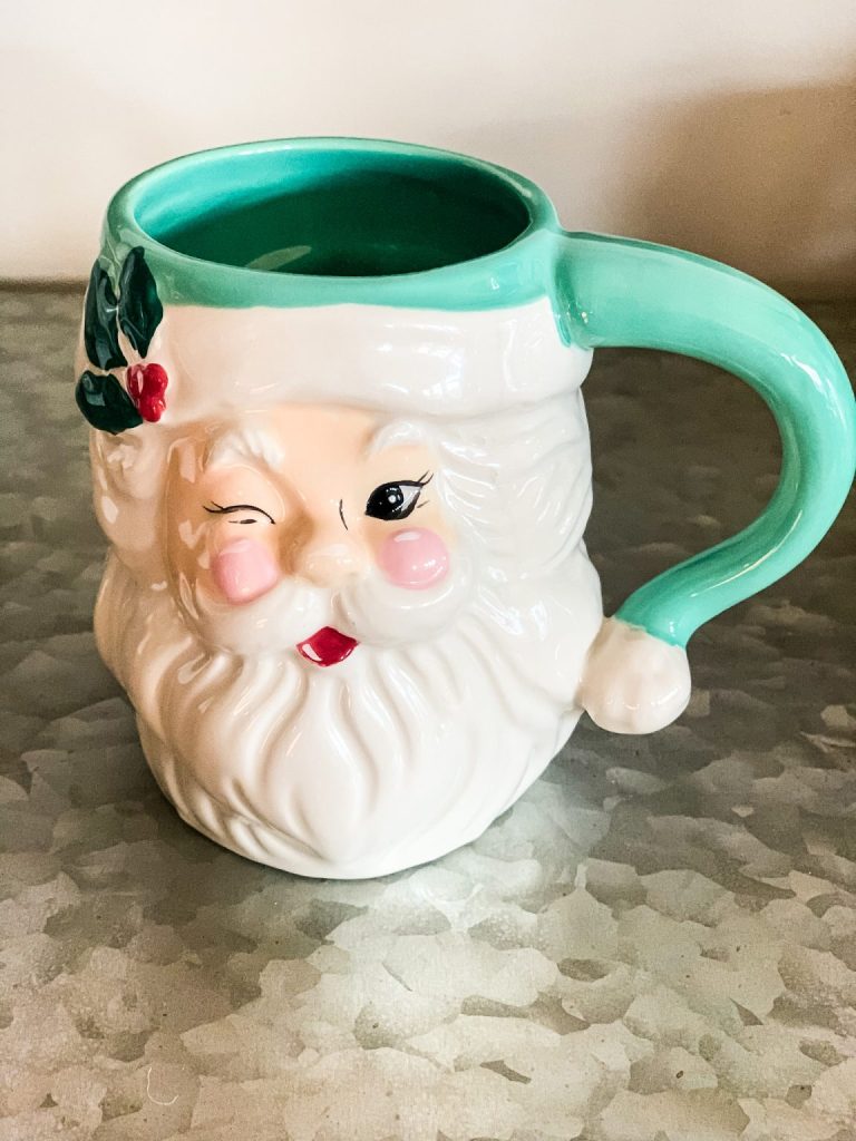 A green and white Santa mug sitting on a table. 