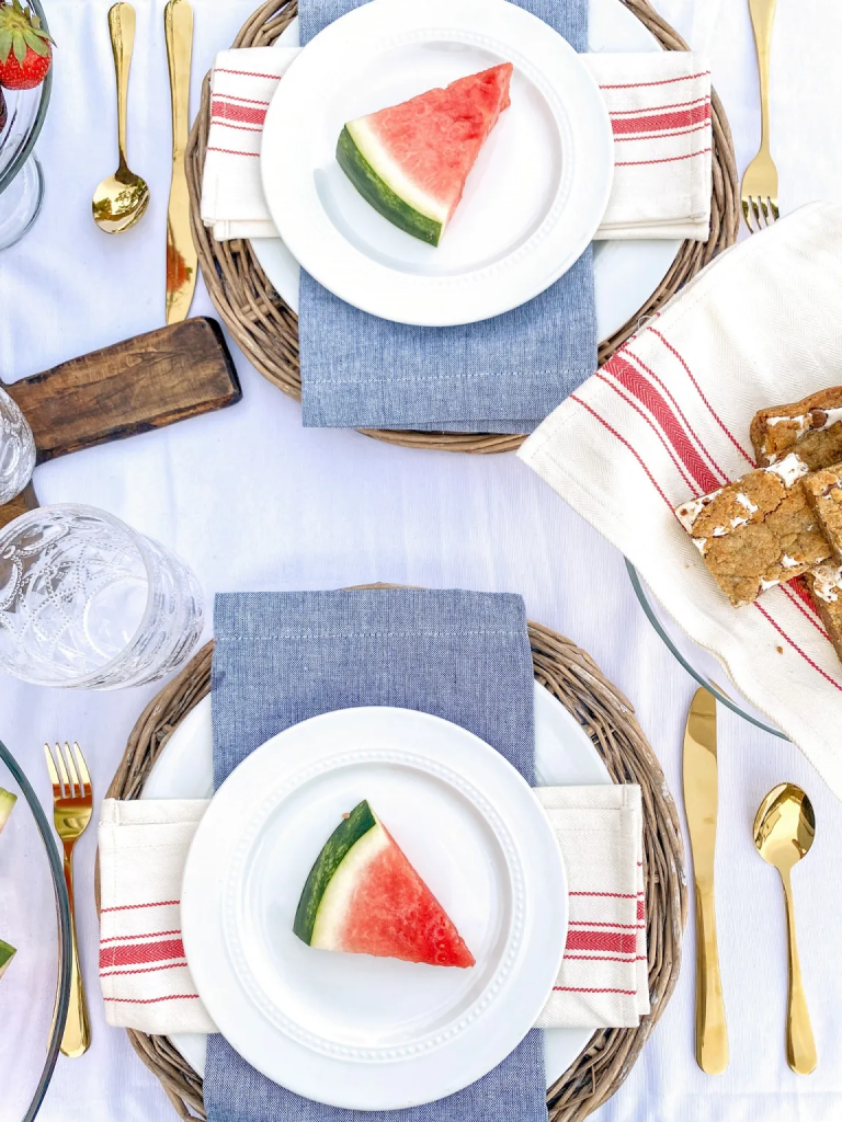 A patriotic table setting with a white table cloth and red, white and blue cloth napkins. Gold flatware was used for this project. 