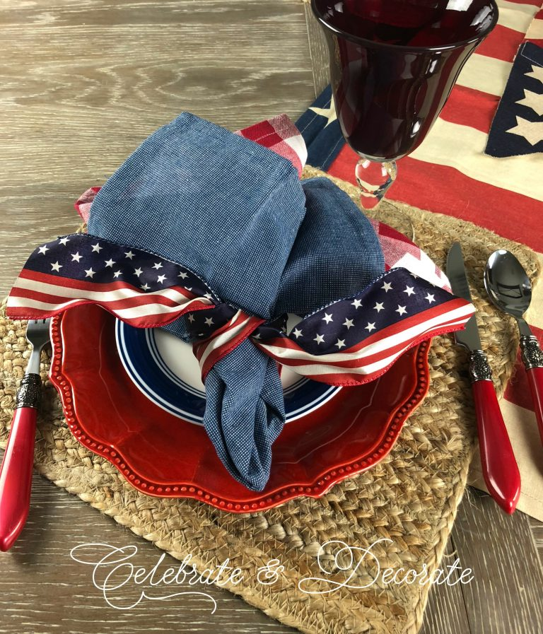 A patriotic table setting with red dinner plates, blue and white salad plates and red handled flatware. 