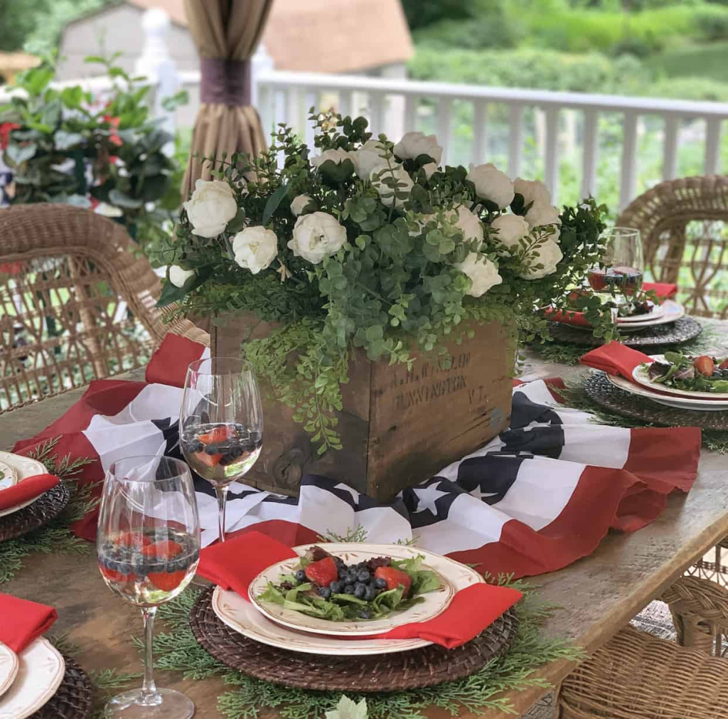 A festive table using an American flag bunting, everyday dishes and a beautiful floral centerpiece in a wooden crate.