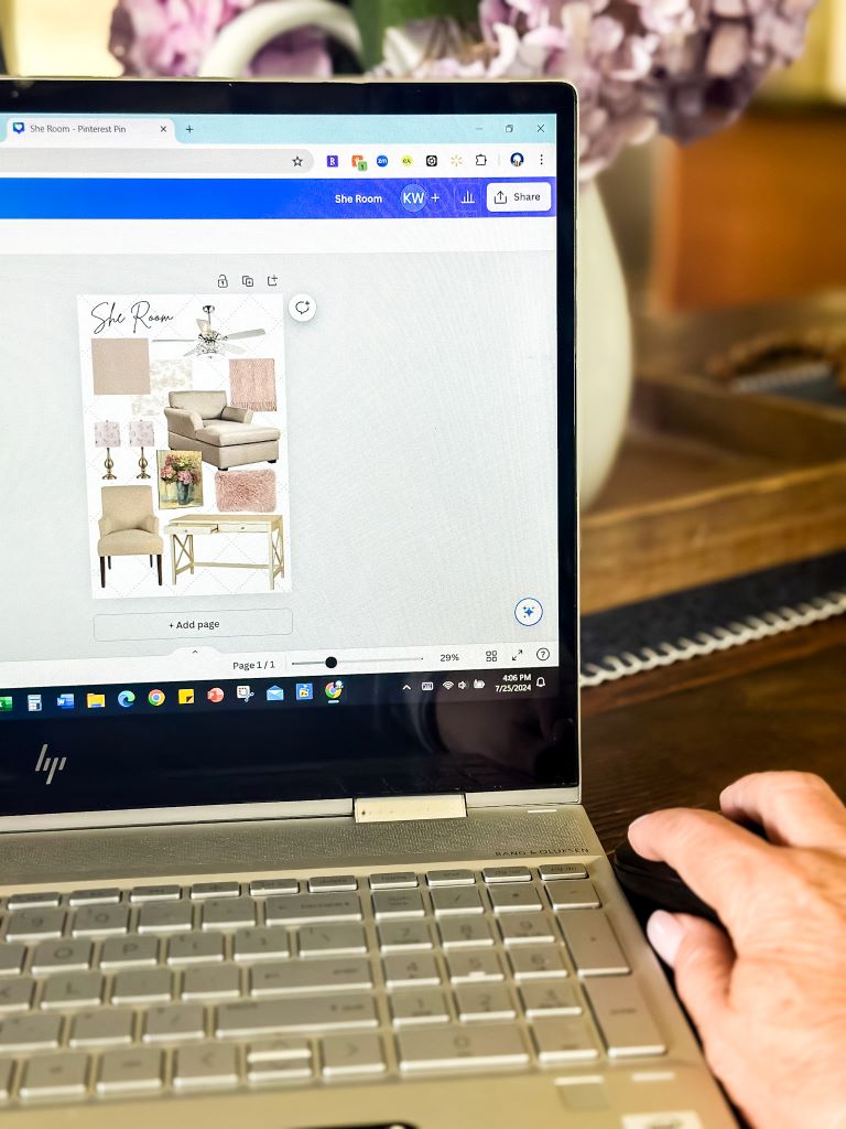 A person's hand hovers over a laptop mouse, with a room design moood board visible on the screen. The mood board shows a collage of furniture, decor, and color palettes.