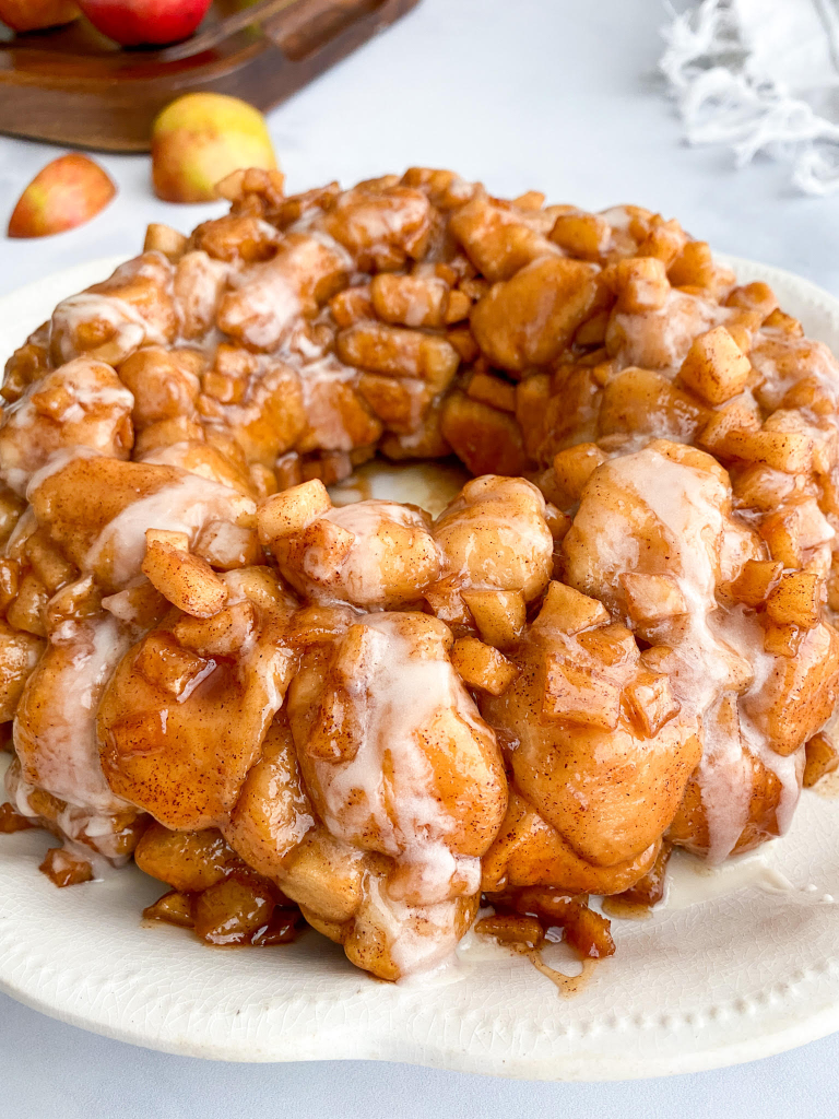 A golden-brown monkey bread with a generous drizzle of white icing, resting on a white plate. The individual dough balls are visible through the glaze.