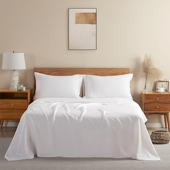 A bed with crisp white linen sheets, a wooden headboard, and matching bedside tables. A framed print hangs on the wall above the bed.