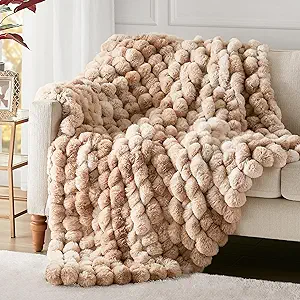 A luxurious throw blanket made of soft, faux fur with a textured pattern of fluffy pom-poms in beige and cream shades.