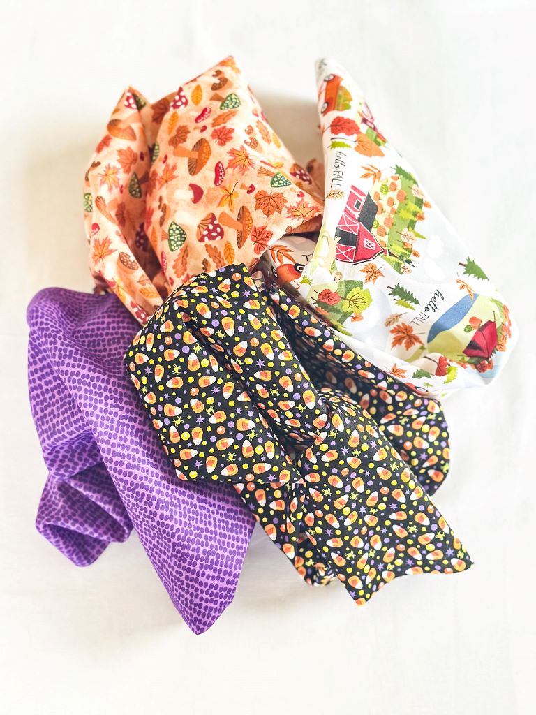 A pile of colorful Halloween-themed fabric. The fabrics feature patterns like candy corn, pumpkins, and fall foliage.