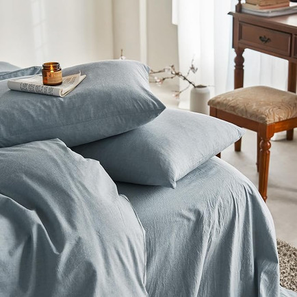 A bed with light blue linen sheets, several pillows, and a book and candle on one of the pillows.