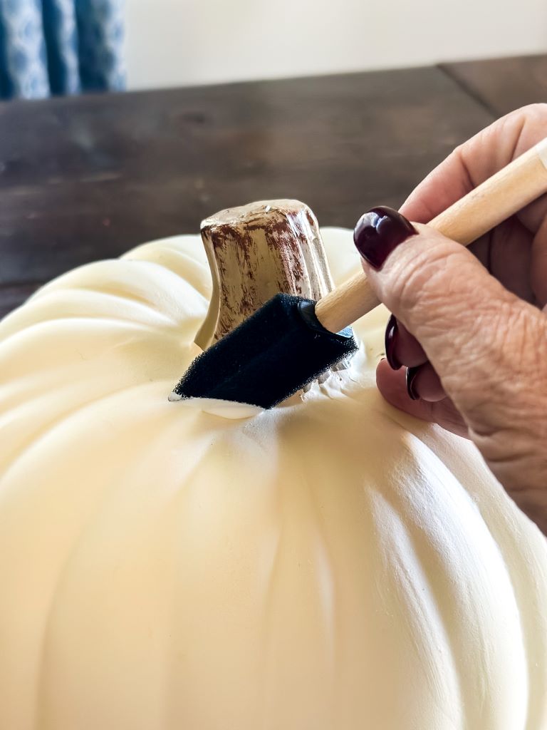 Applying mod podge to a white craft pumpkin with a small foam brush. 