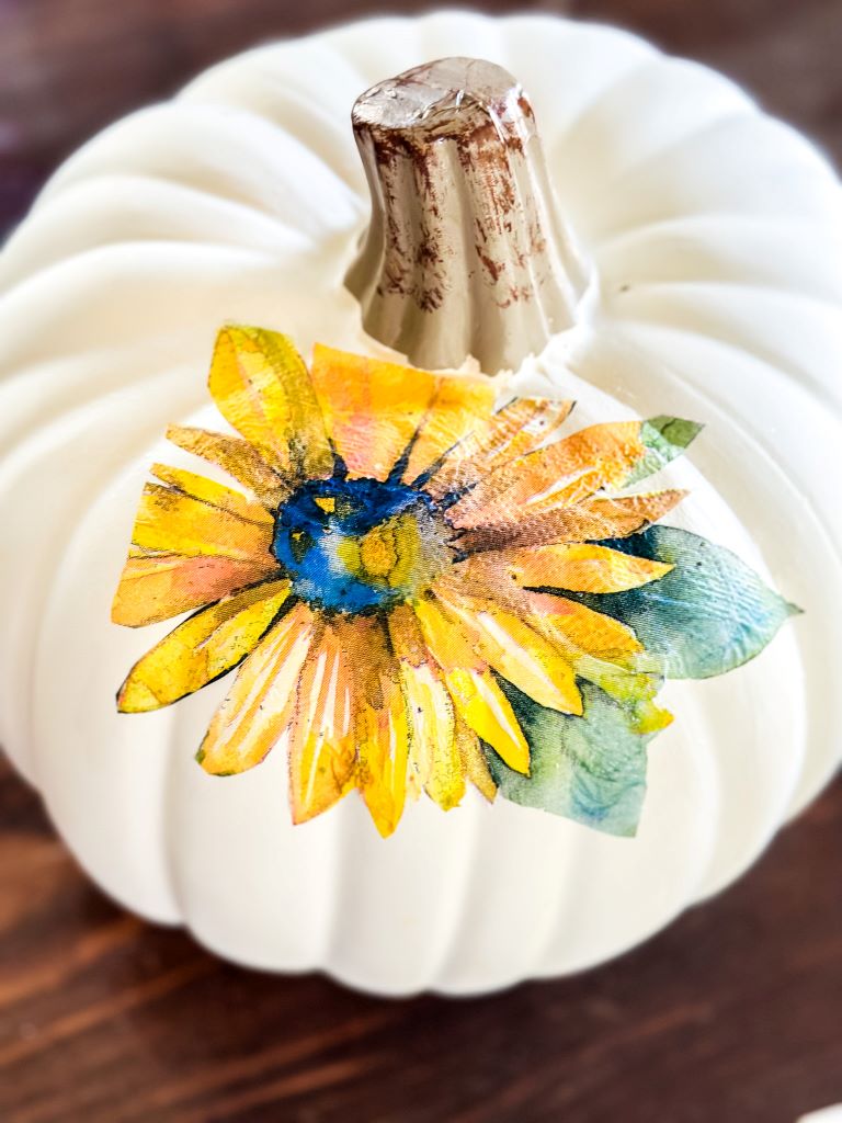 A white craft pumpkin with a cut out sunflower from a napkin. Mod Podge was used to adhere the sunflower. 