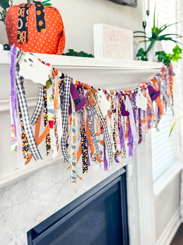 A rag Halloween garland with wooden purple witch hats and wooden white ghosts hanging on a white mantel decorated for Halloween.