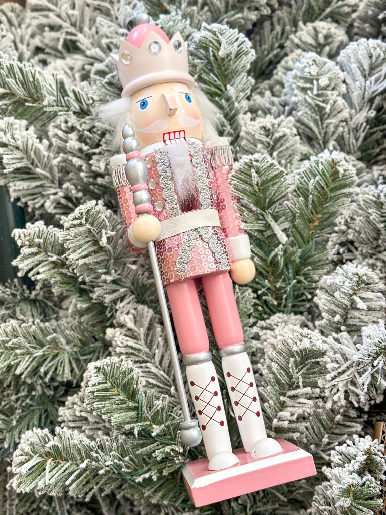 A King of Christmas tree with a pink and sequin Nutcracker sitting on top of it in the box. 