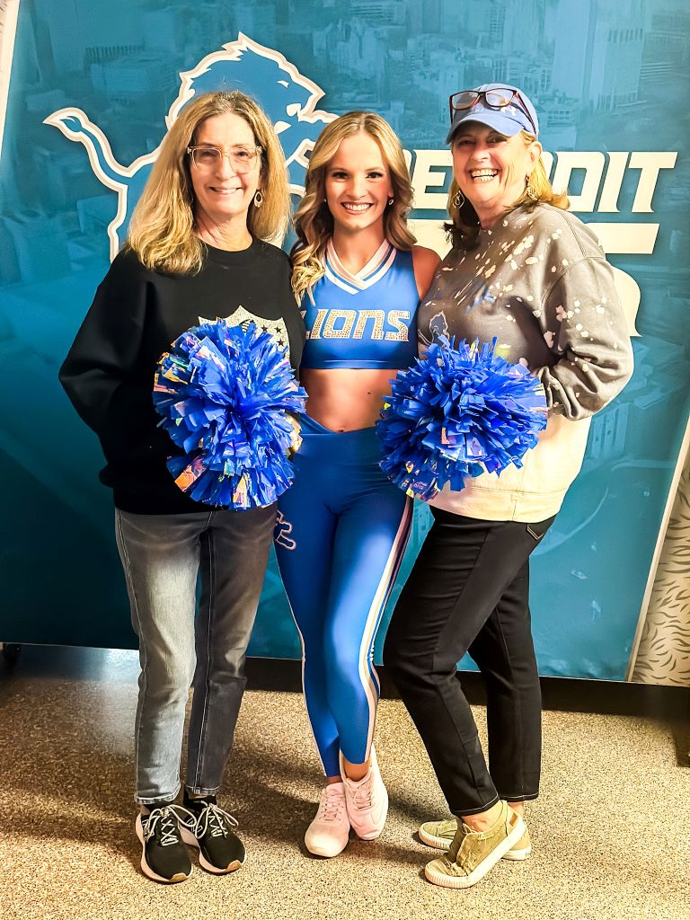 Three friends at a Lion's football game, holding pom poms.