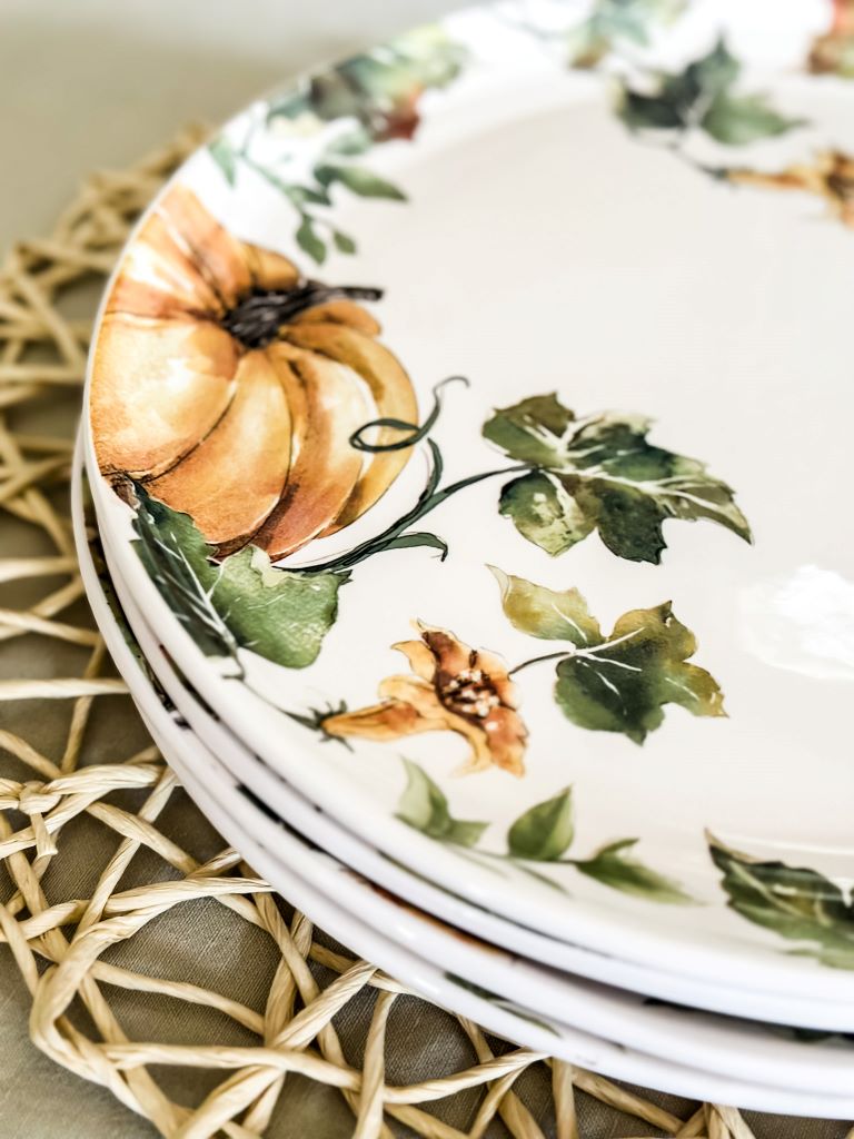 White plates with pumpkin and vine designs stacked on woven placemats. 