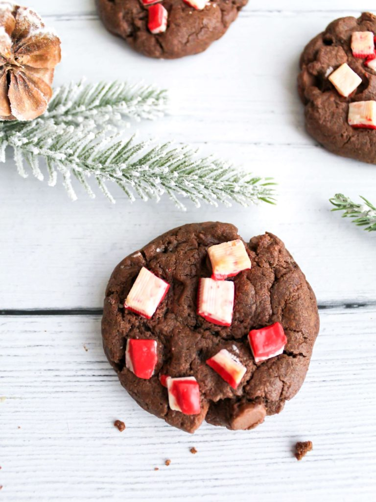 Double chocolate chip peppermint cookies on a white table with pinecones and pine branches.