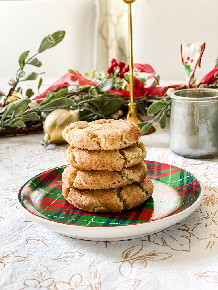 A stack of four eggnog snickerdoodle cookies on a red and green plaid plate, with Christmas decorations in the background.