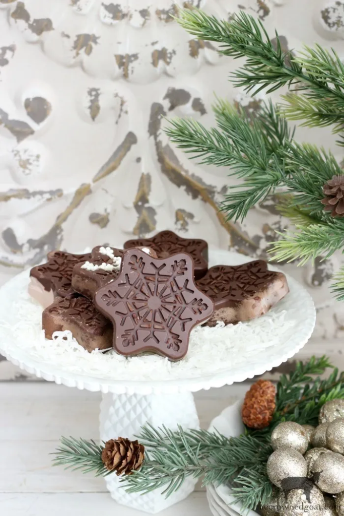 A plate of homemade chocolate snowflake cookies, surrounded by pine branches and ornaments.