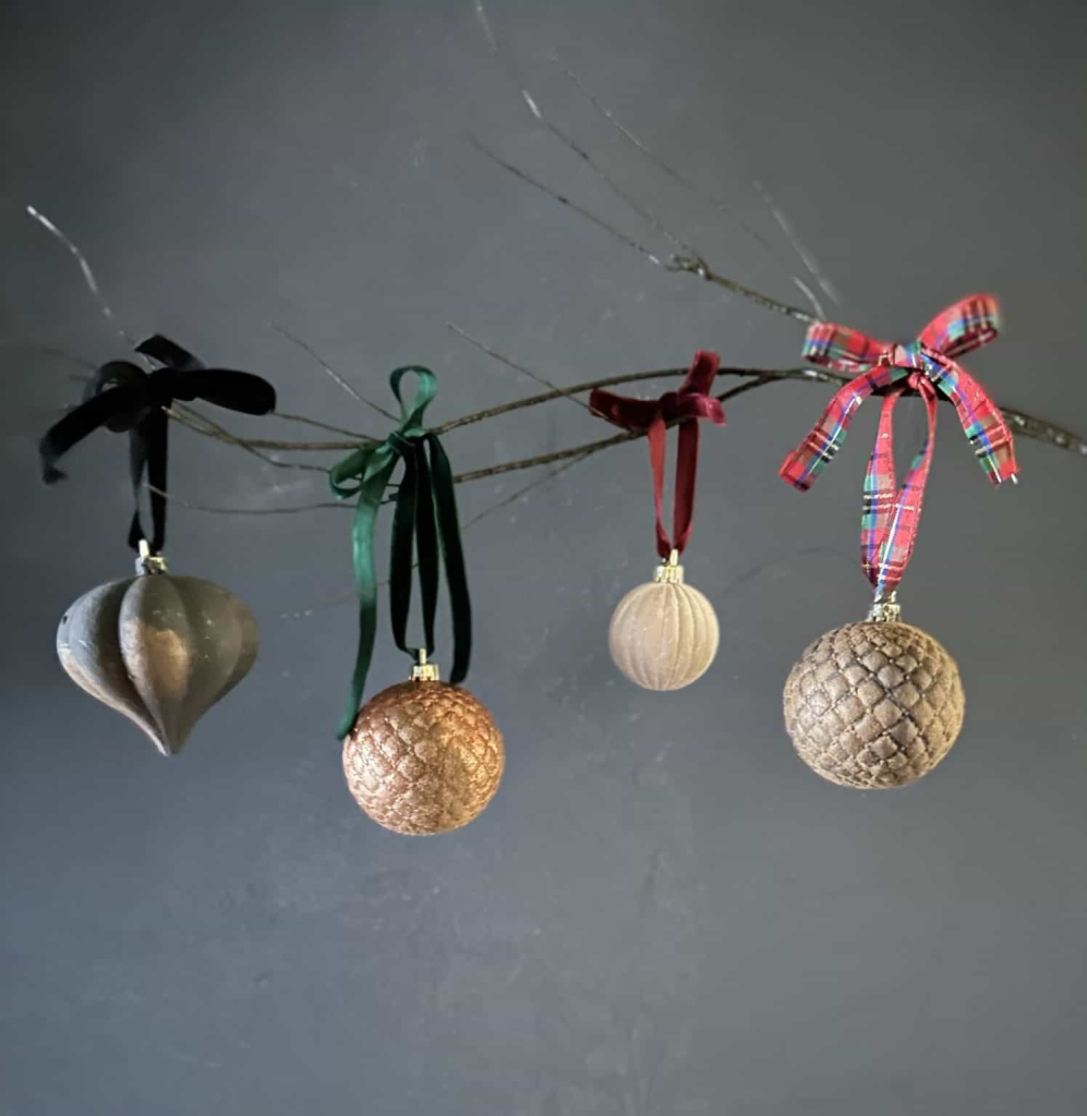 Four painted ornaments on a twig tied with ribbon.