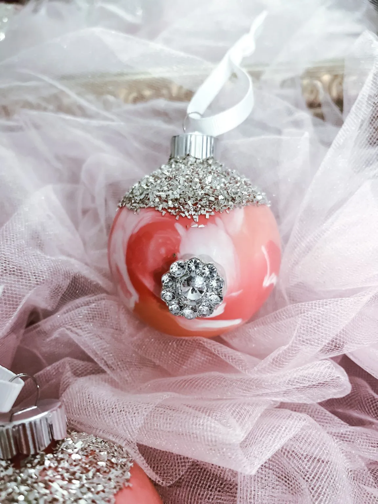 A marbleized Christmas bulb with German glass glitter and a rhinestone embellishment sitting on a piece of white netting fabric.