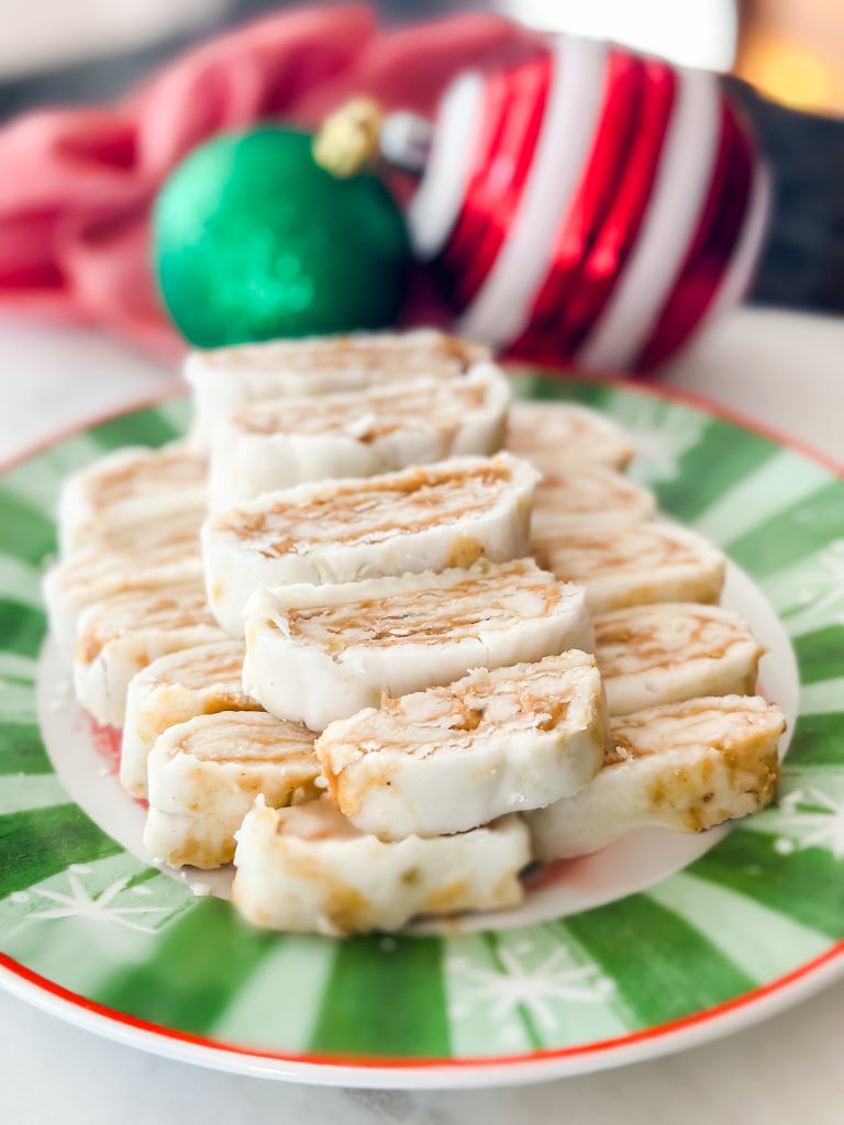 A green and red Christmas plate with homemade peanut butter candy. There is a red cloth napkin and ornaments in the background. 