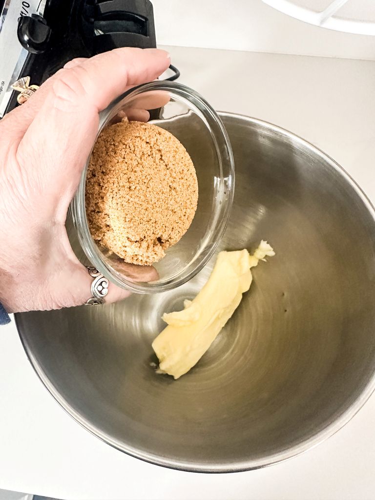 Brown sugar being added to butter in a silver mixing bowl.