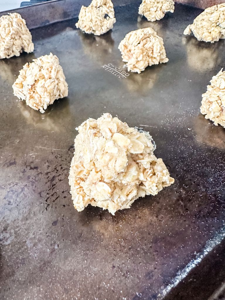 Scoops of raw cherry oatmeal cookie dough arranged on a dark metal baking sheet before going into the oven, a simple baking step for a Michigan-inspired treat.
