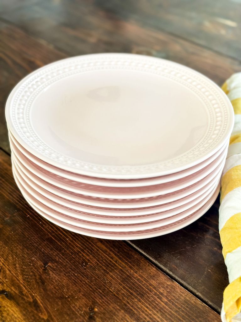 A stack of light pink dinner plates set on a wooden table. 