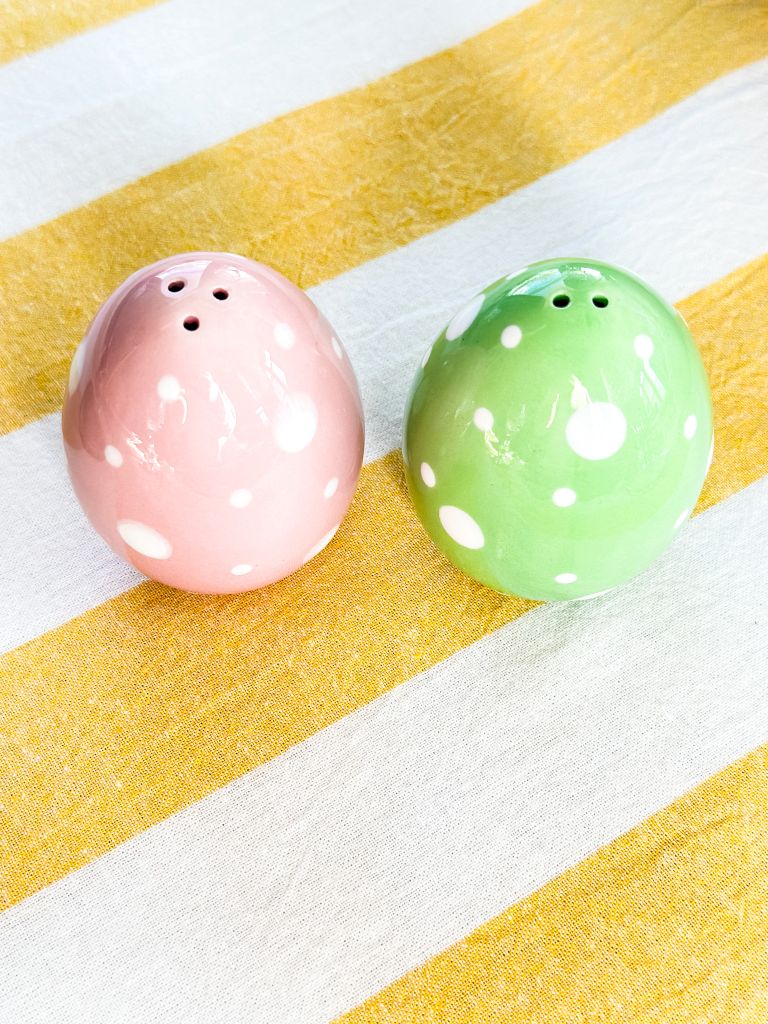 Pink and green salt and pepper shakers sitting on a yellow and white table runner. 