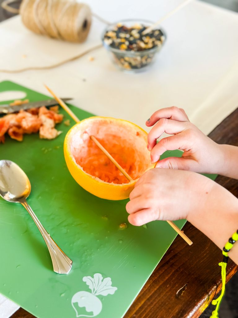 Inserting wooden skewers into a hollowed-out grapefruit on a green cutting board.