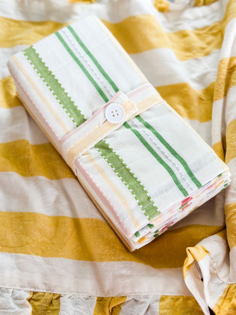A white and yellow table runner with cloth napkins that are striped with green, pink and yellow. 