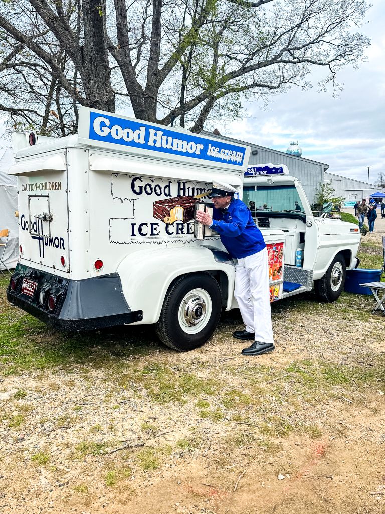 A vintage white Good Humor ice cream truck with a blue logo and a person dressed in a uniform serving ice cream.