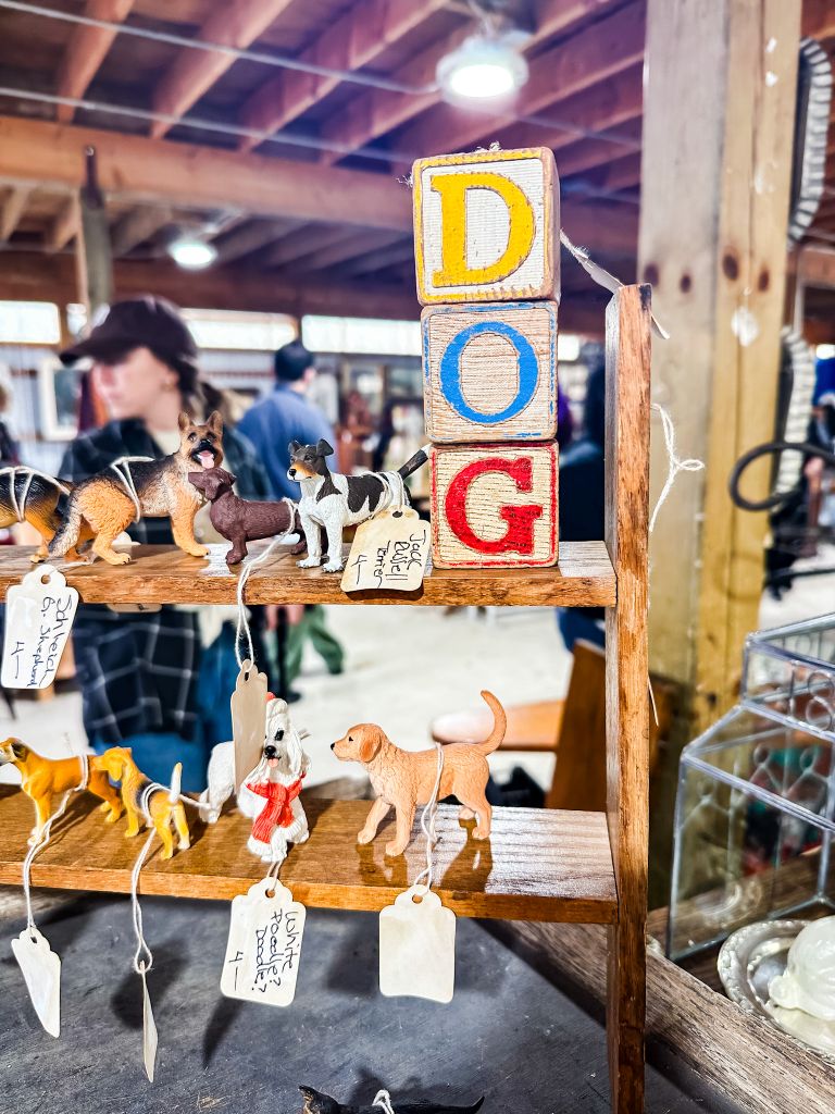 A small wooden shelf displays vintage toy dogs and wooden blocks spelling 'DOG' at a vintage  market.