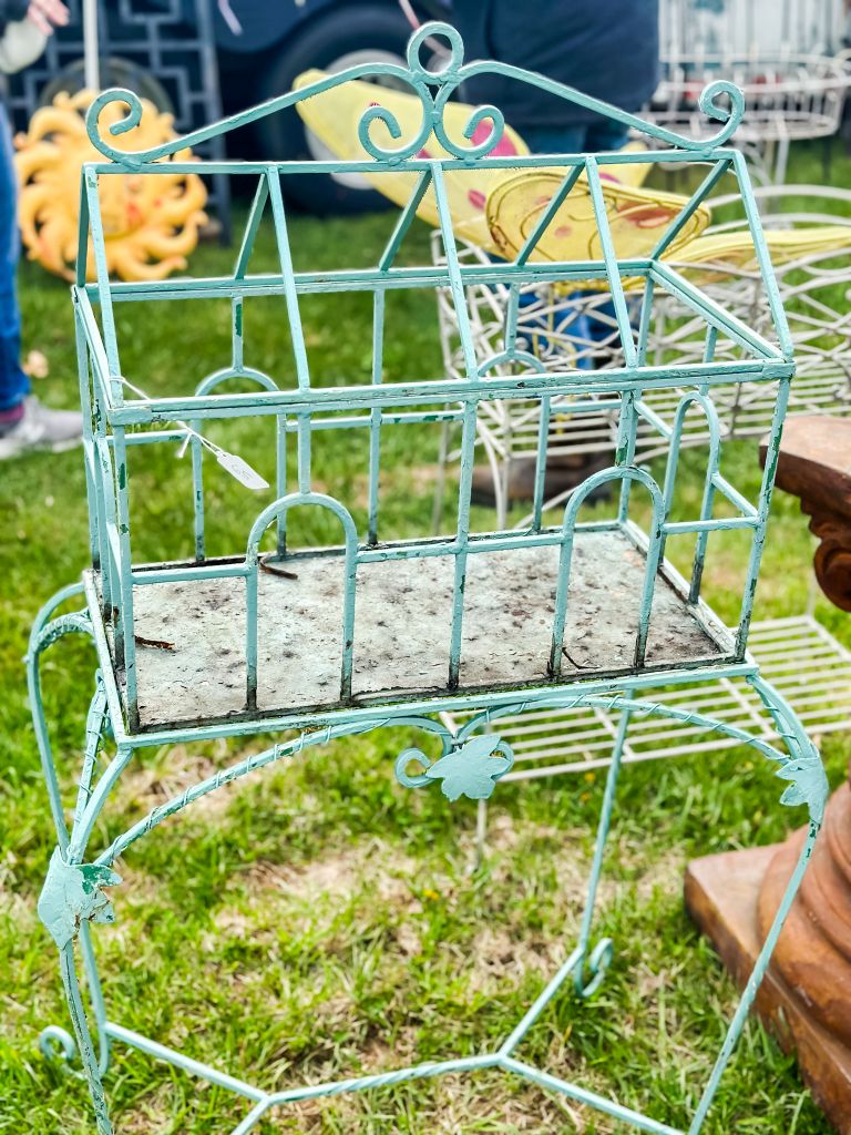 Close-up of an ornate, turquoise-painted wire cage, possibly for plants or birds, at a flea market.