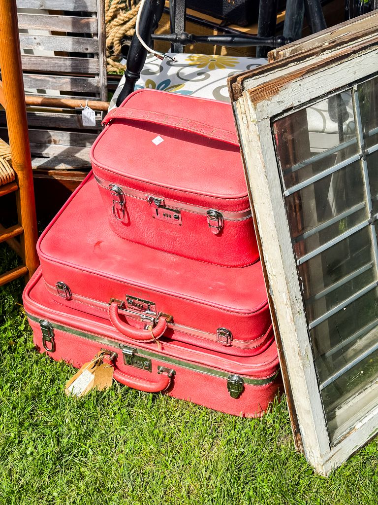 A stack of three vintage red suitcases on the grass at an outdoor market.