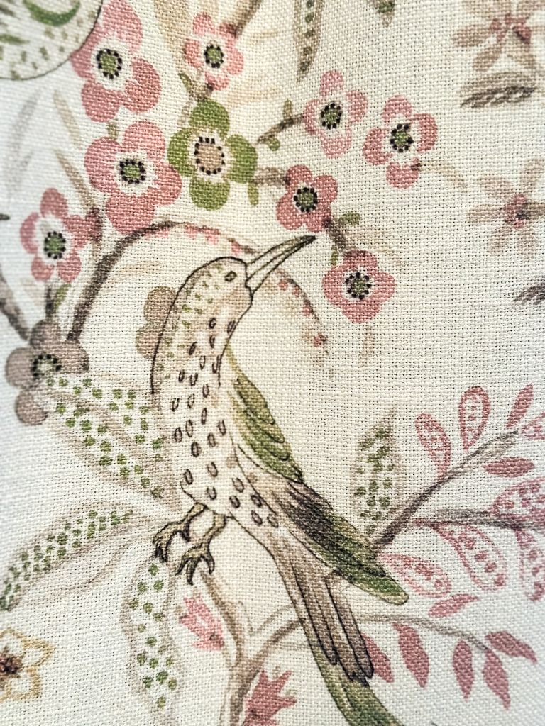 Close-up of fabric featuring a detailed bird perched on a branch with pink and green floral patterns.
