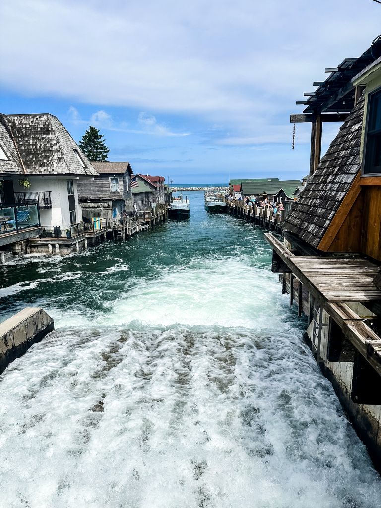Historic Fishtown in Leland, Michigan, showing the working shanties and fishing boats lining the Leland River with water rushing over a dam in the foreground.