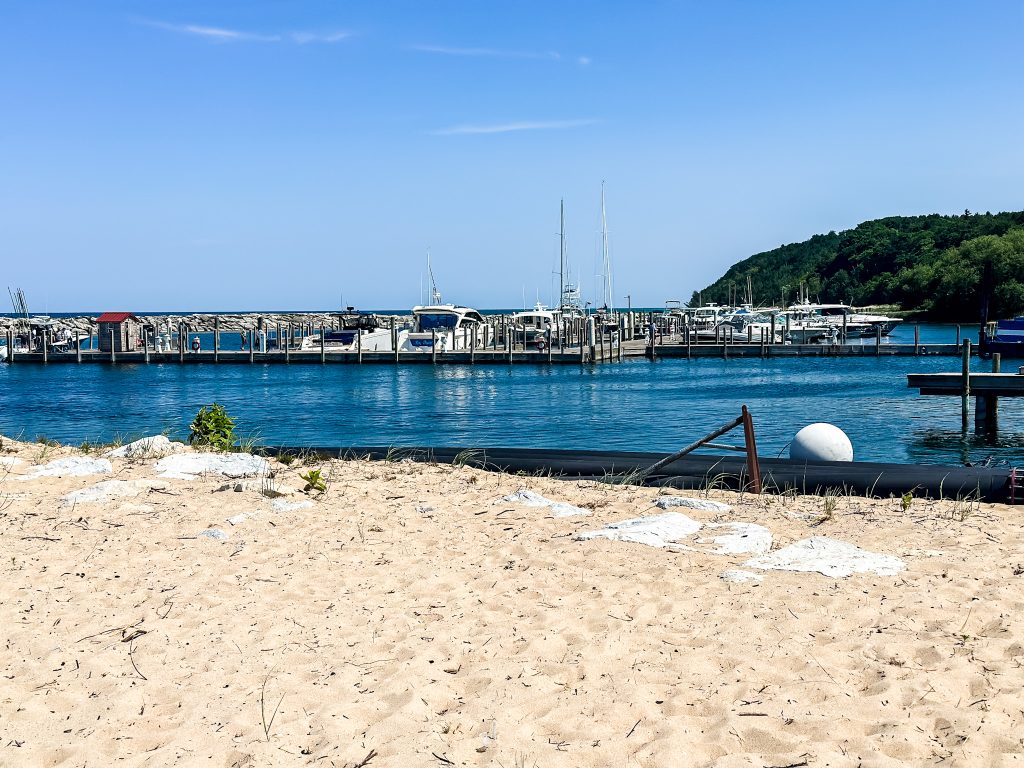 Leland Michigan marina in Fishtown with boats docked along the pier and sandy beach in the foreground on a sunny summer day.