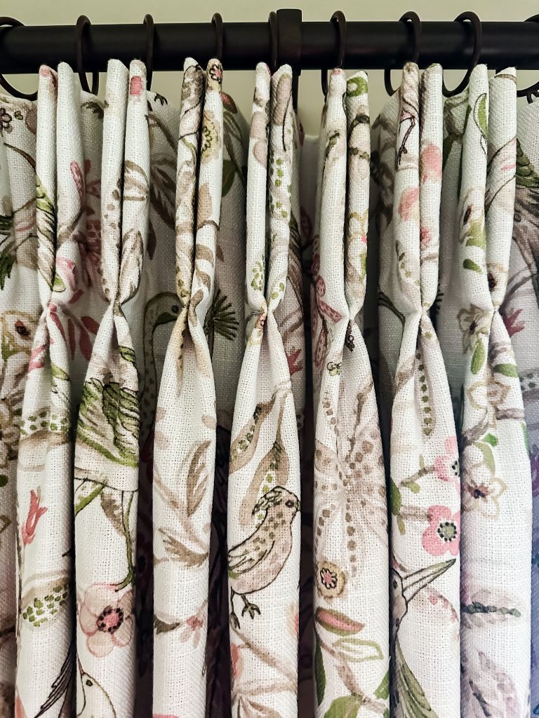 Close-up of pleated floral curtains with a bird and botanical print, from TheHue hanging from a dark curtain rod with rings.