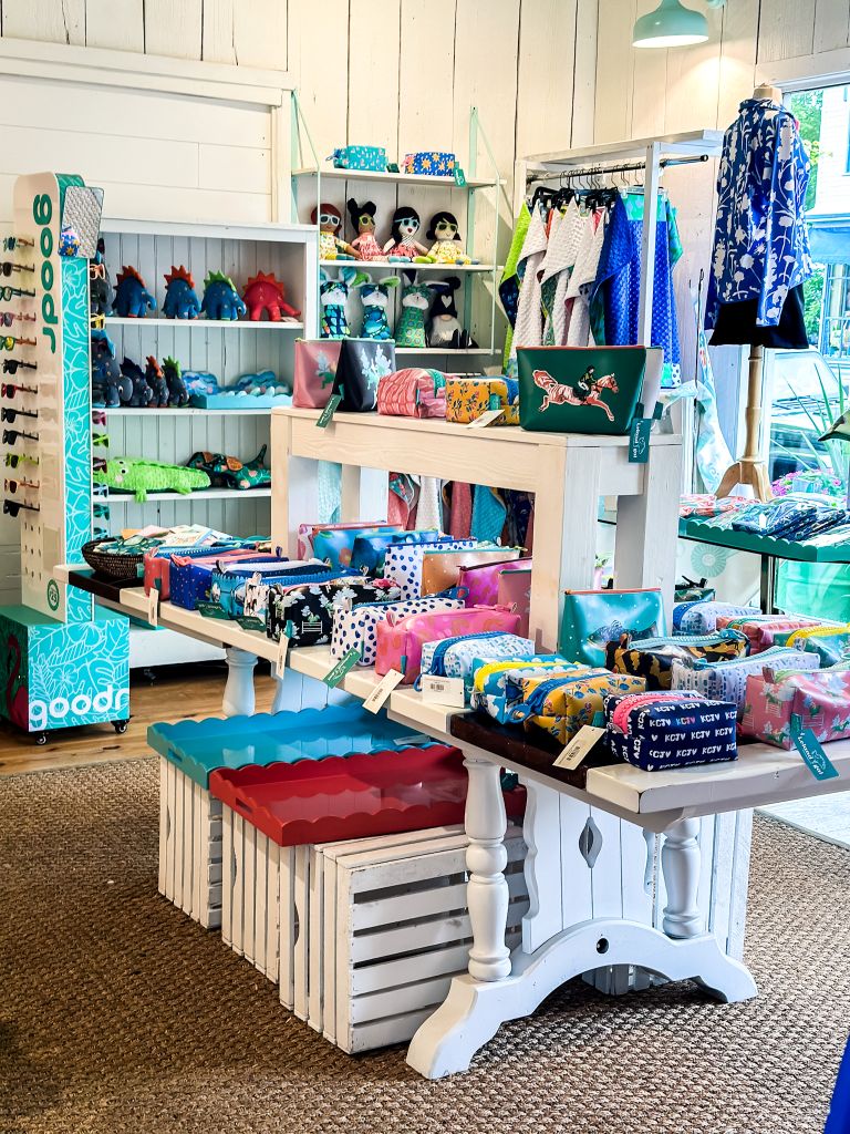 Colorful boutique shop interior in Fishtown Leland Michigan displaying Goodr sunglasses, printed pouches, stuffed animals, and clothing.