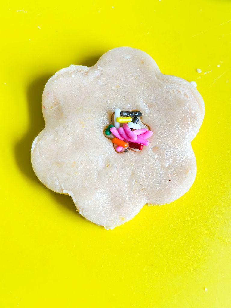 Raw sugar cookie dough in the shape of a flower with colorful sprinkles in the center.