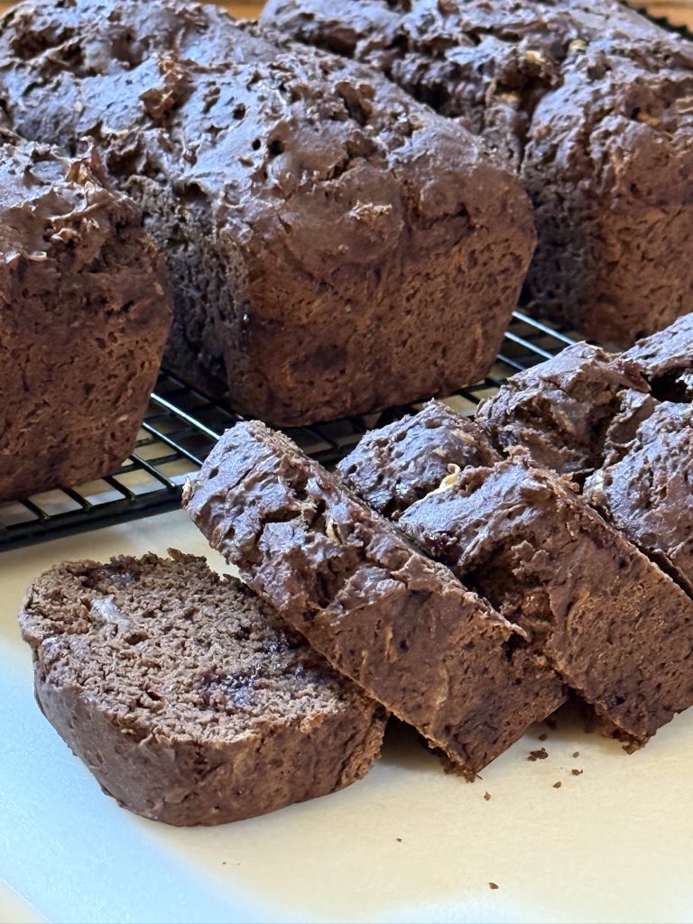Sliced homemade double chocolate zucchini bread with chocolate chips, displayed on a wire rack.