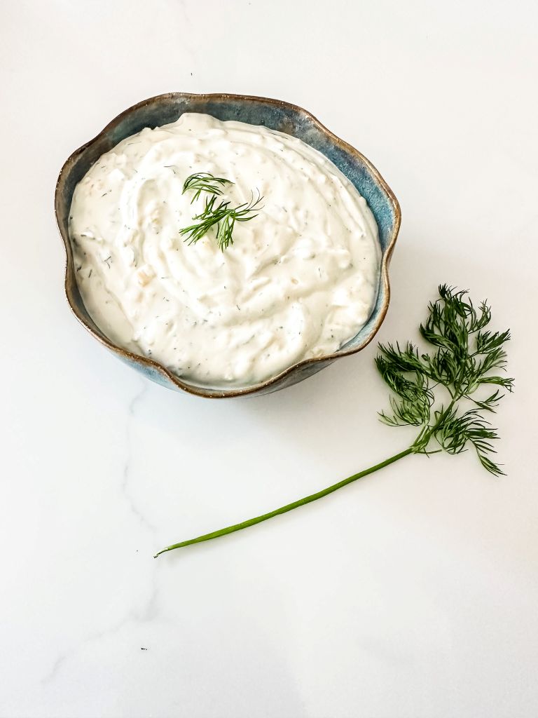 Creamy homemade dill dip in a blue ceramic bowl, garnished with fresh dill, on a white marble countertop.