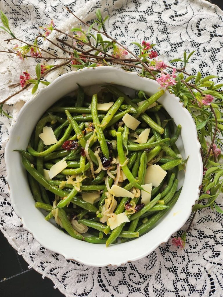 Delicious bowl of vegetarian green beans with garlic, shallots, cranberries, and shaved Parmesan cheese.