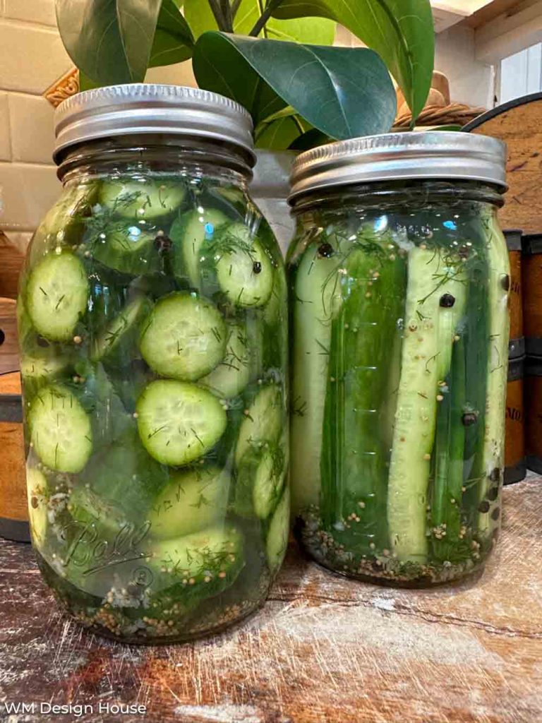 Two glass canning jars filled with homemade dill pickles, one with cucumber slices and the other with whole spears.